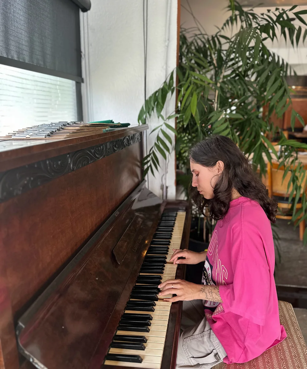 Karen toca um piano de armário de madeira escura.