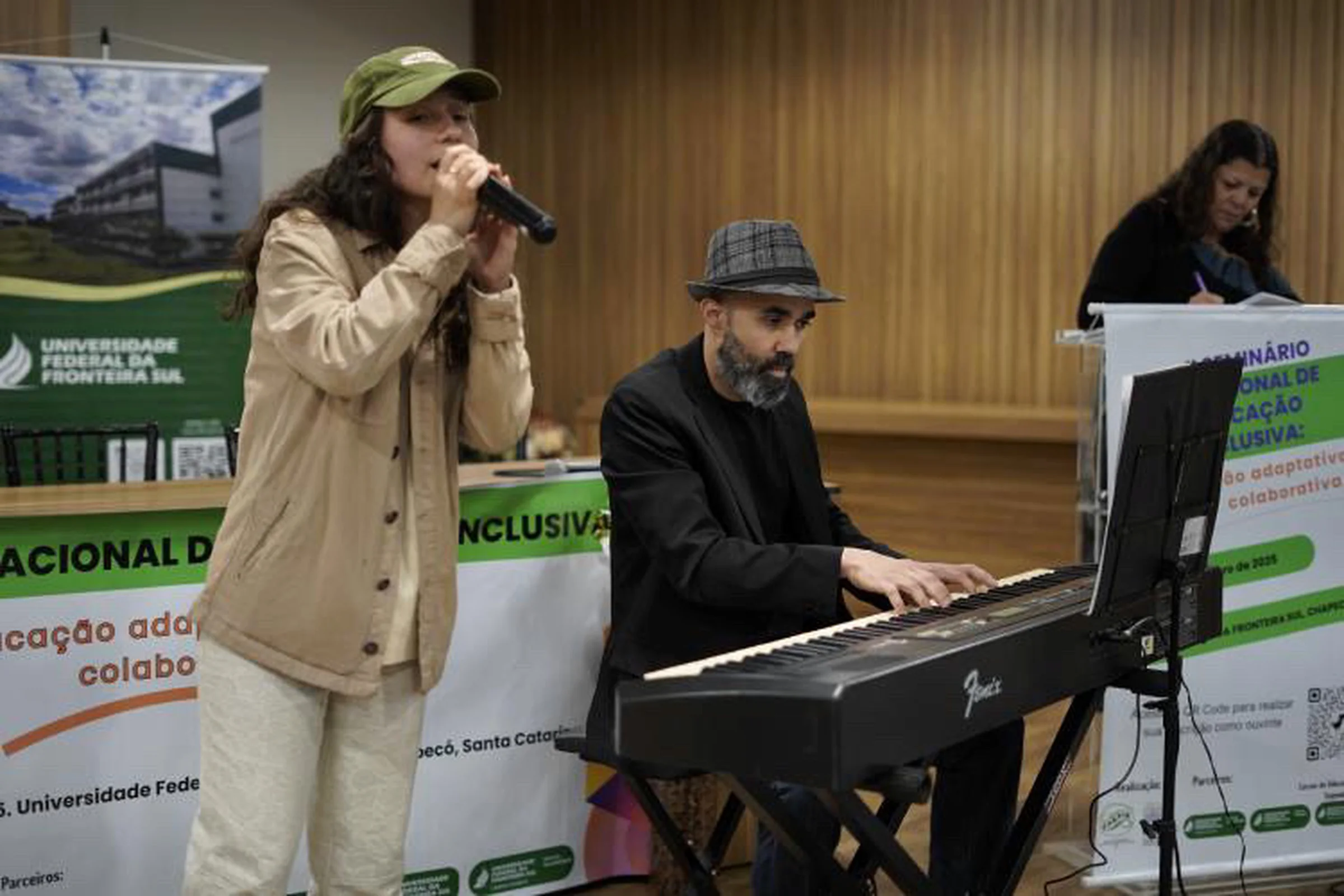 Karen canta ao microfone ao lado de um tecladista, no seminário da UFFS.