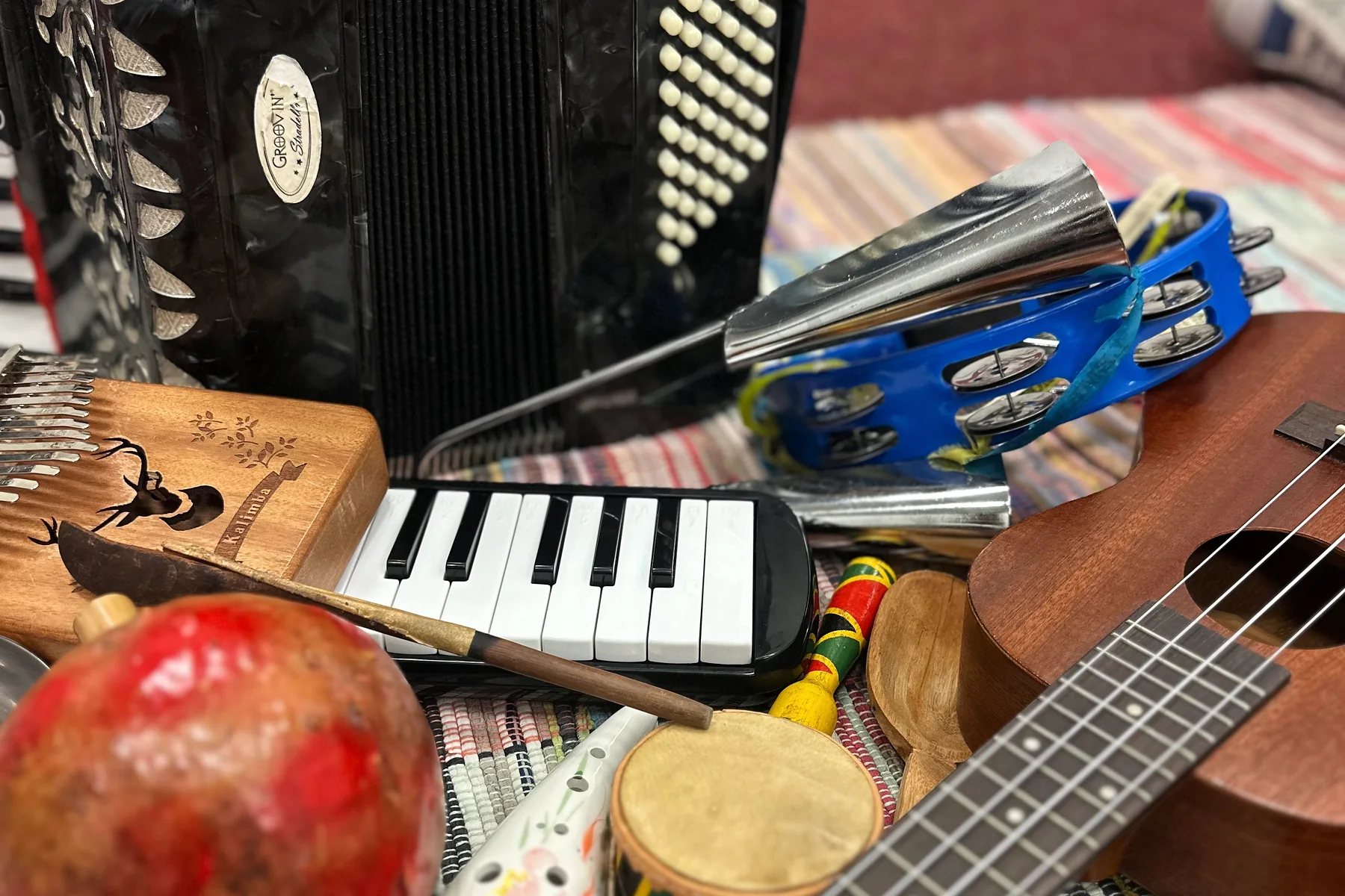 Instrumentos de aula sobre um tecido listrado: acordeão, escaleta, ukulele, pandeiro, kalimba e chocalhos.