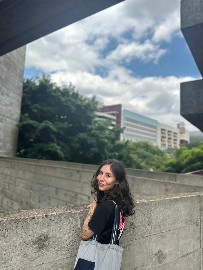 Karen encostada num muro de concreto, sob o céu aberto.