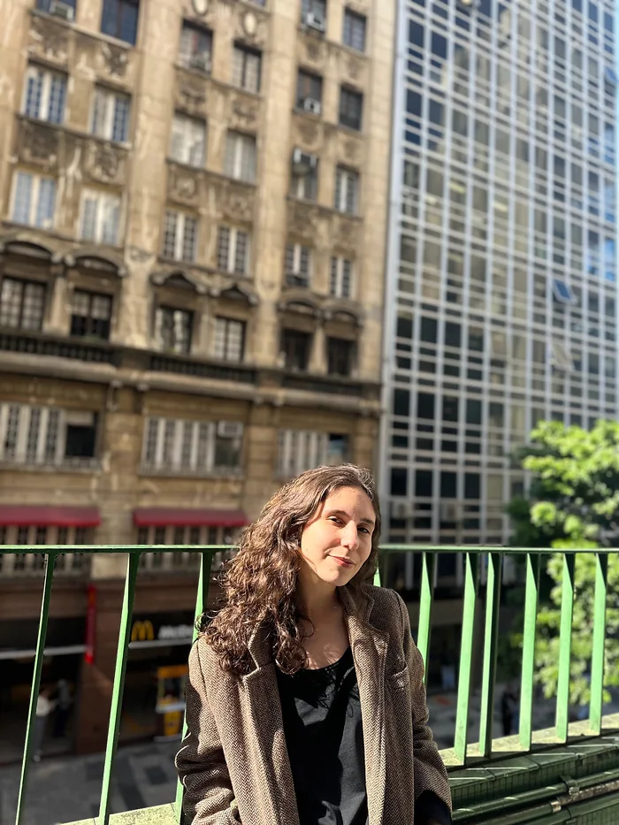 Karen numa varanda entre prédios antigos e modernos.