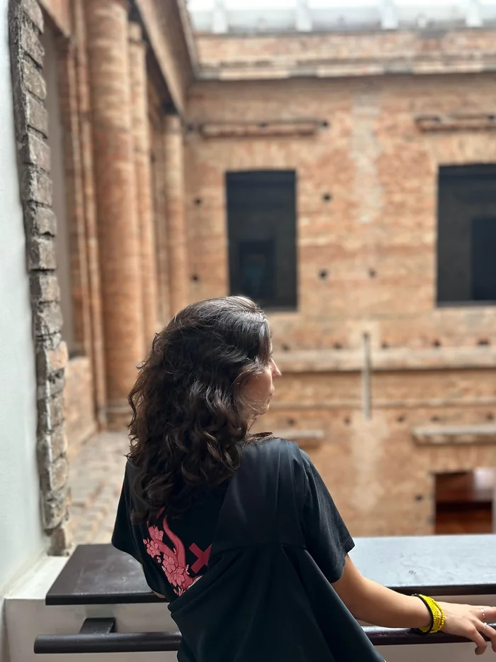 Karen junto a uma janela, diante de uma fachada de tijolos.