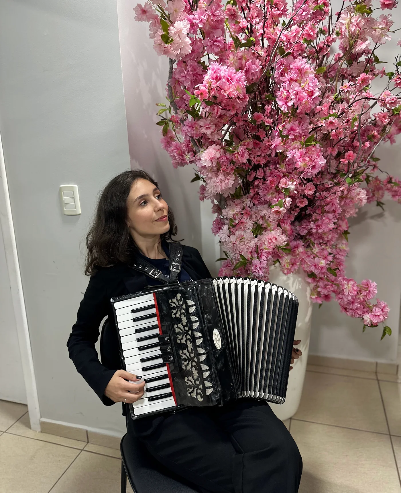 Karen toca acordeom ao lado de um arranjo de flores cor-de-rosa.